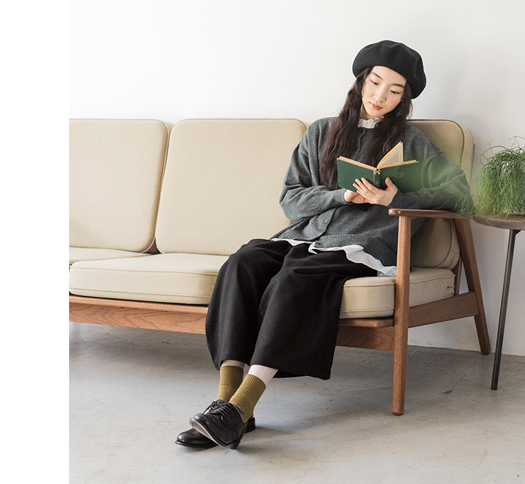 ウールミックスガウチョパンツ（ブラック）を着た女性がソファに座って本を読んでいる